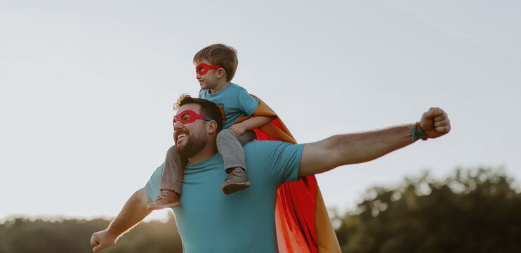 Father and son in red capes enjoy outdoor adventure with playful heroic spirit