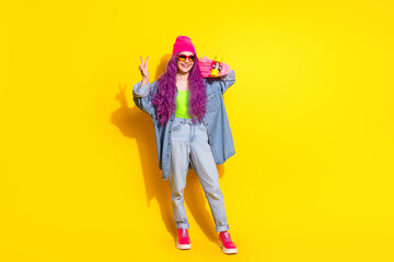 Young stylish woman with vibrant pink hair in casual yellow and denim wear posing with skateboard on a yellow backdrop