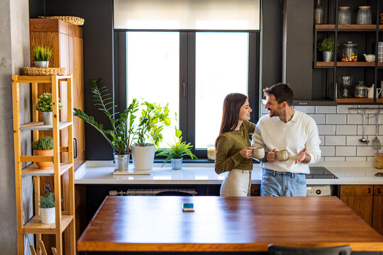 Young couple enjoying a cozy morning in their modern kitchen, chatting and sipping coffee together, radiating love and happiness