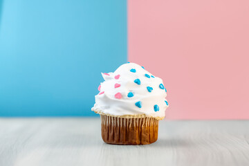 Gender reveal cupcake with blue and pink heart sprinkles on colorful background