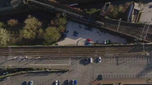 Aerial view of Manchester, UK, showing train tracks, roads with vehicles, a canal bordered by trees, and visible construction activity.