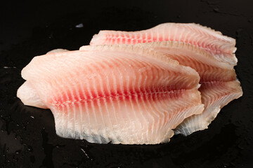 Fresh tilapia fillet on black background, top view.