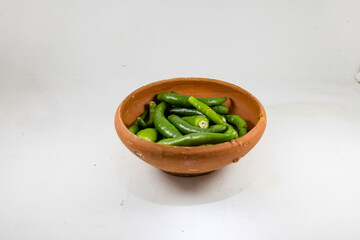 A collection of fresh green chilies displayed in a handmade clay bowl on white background