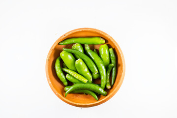 A collection of fresh green chilies displayed in a handmade clay bowl on white background