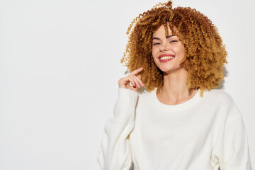Smiling woman with curly hair, wearing a white sweater, against a plain white background, exuding...