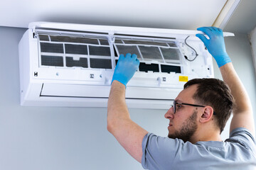 A Skilled Technician Performing Maintenance on an Air Conditioning Unit While Wearing Blue...