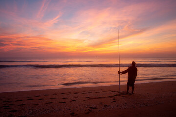 Colorful sunrise on the beach with fisherman in foreground