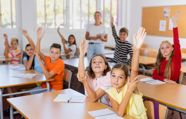 Group of happy school pupils raise their hands up in classroom during lesson in school