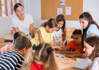 Young female teacher and happy schoolkids playing interesting learning board game during lesson in classroom
