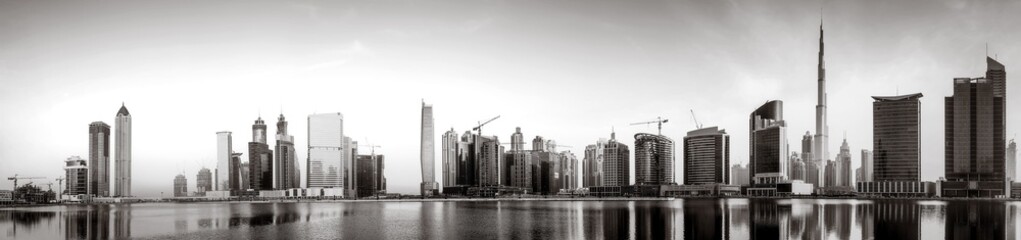 Fototapeta premium Monochrome city skyline with tall skyscrapers reflecting on calm water under a cloudy sky, Dubai Marina bay UAE