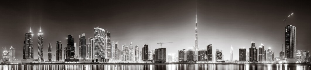 Fototapeta premium Monochrome city skyline with tall skyscrapers reflecting on calm water under a cloudy sky, Dubai Marina bay UAE