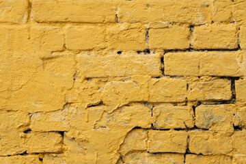 A textured yellow brick wall reveals signs of wear and age, showcasing a vibrant yet weathered appearance, typical of urban architecture during daylight hours
