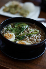 Ramen soup in black plate on wooden table in café. Vertical photo