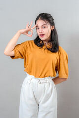 Portrait of a smiling young Asian woman making an OK hand gesture while looking confident and positive. Her friendly facial expression radiates charm, joy, and assurance.
