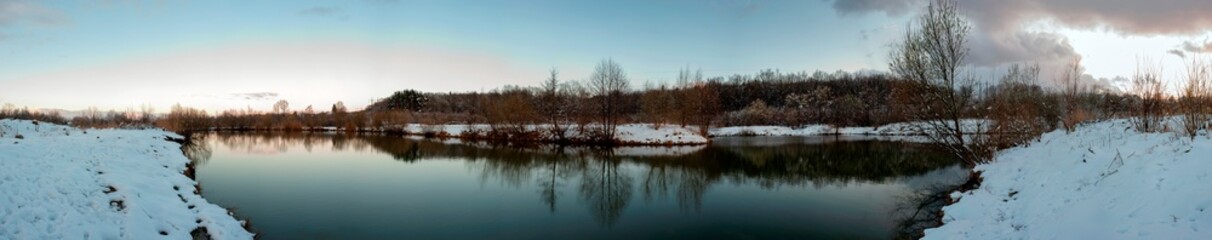Fototapeta premium Panorama of the sunrise over the winter river. The sun rises over the lake. Autumn frost. The frozen river is covered with thin ice, the grass glistens with frost.