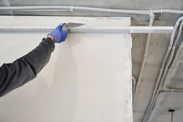 A male plasterer holds a metal rule in his hands and smears plaster on the wall. High quality photo