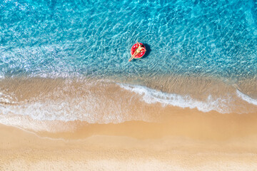Naklejka premium Aerial view of a young woman swimming with red swim ring in blue sea with waves at sunset in summer. Tropical landscape with girl, clear water, sandy beach. Top view. Vacation. Sardinia island, Italy