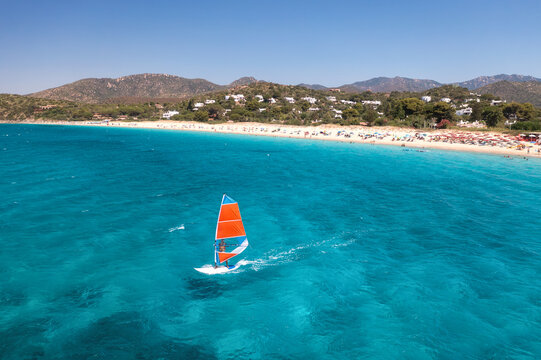 Aerial view of windsurfer on blue sea at sunny summer day. Windsurfing. Extreme sport and vacation. Top view of man on windsurfer board, waves, clear azure water in Sardinia, Italy. Tropical landscape - Powered by Adobe