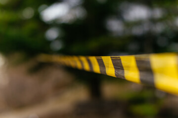 A close-up of a yellow and black caution tape stretched across an outdoor scene, symbolizing...