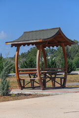 Wooden gazebo invites relaxation in a serene park under a clear blue sky during a sunny afternoon
