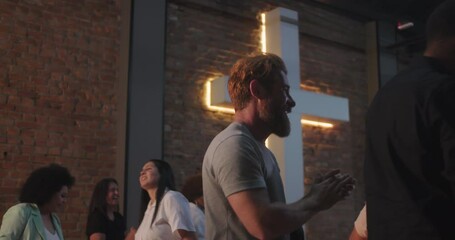 Group of diverse people clapping hands and dancing during church worship service, expressing joy and faith with glowing cross in background
