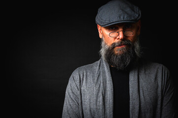Portrait of an emotional bearded man in a gray hat, gray sweater and glasses looking at the camera...