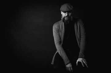Black and white, portrait of an emotional bearded man in a gray hat, gray sweater and glasses...