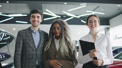 Happy car dealership team standing together with customers in an automotive showroom during daytime, smiling and engaging