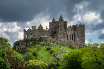 Fototapeta premium Discover the stunning, iconic Rock of Cashel, a remarkable medieval castle perched on a hill in Ireland, beautifully surrounded by lush greenery and breathtaking skies