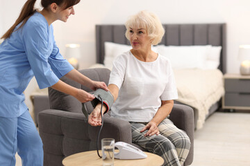 Nurse measuring senior woman's blood pressure at home