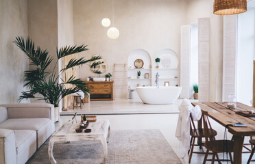 Luxurious spa-like bathroom featuring freestanding white bathtub tropical palms and natural wooden elements. Minimalist design with cream walls pendant lights and shelving creates peaceful ambiance