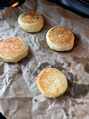 Four round crusty cakes are cooking on parchment paper in a warm kitchen. The golden-brown top suggests a delicious flavor and homemade charm. Perfect for a weekend brunch