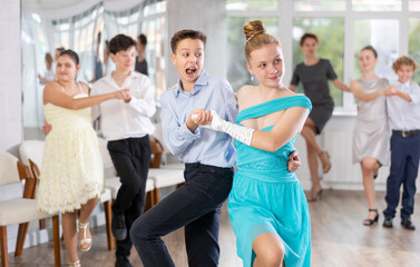 Naklejka premium Positive teen boy and girl are dancing contemporary modern discofox in couple during lesson at studio. Leisure activities and hobby for positive people.