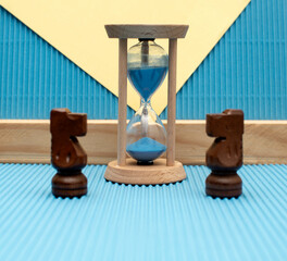 Hourglass with a flowing blue sand inside and wooden chess knights