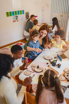 Diverse group of preschool children engage in a nature-based learning activity with two teachers, using wood and natural objects to explore creativity and tactile skills in the classroom.