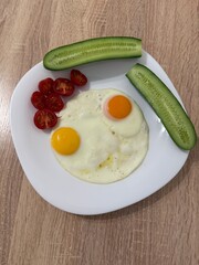 Fried eggs with fresh cucumbers and cherry tomatoes on white plate breakfast meal healthy food concept funny smiley face arrangement  
