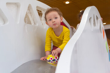 A pretty curly child plays a slide in a game center