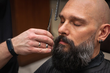Close-up of a barber trimming a beard with electric clippers in a modern barbershop. Professional...