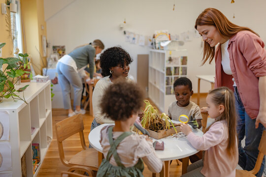Group of diverse preschool children learning gardening with teachers, exploring soil and plants in a fun, hands-on classroom activity.