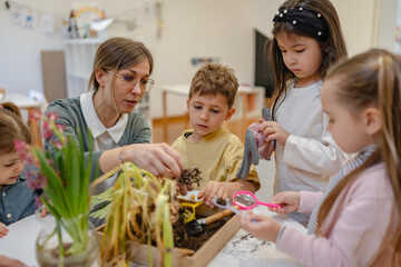 Teacher and curious children explore soil and plants in a classroom science activity, encouraging...