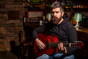 Obraz premium Play the guitar, singer, sing. Beard hipster man sitting in a pub. Live music. Guitars and strings. Bearded man playing guitar, holding an acoustic guitar in his hands