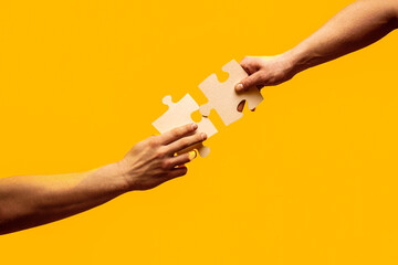 Teamwork concept. Close Up hand of connecting jigsaw puzzle. Two hands trying to connect couple puzzle piece on yellow background