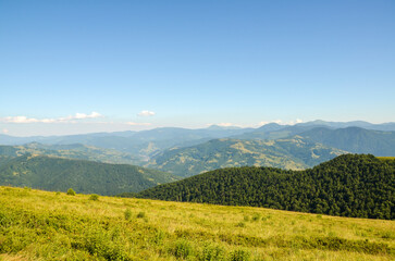 Obraz premium Peaceful natural hillside scene featuring lush grass and trees, scenic mountain ranges extending into the distance, with clear blue skies. Carpathian Mountains, Ukraine 