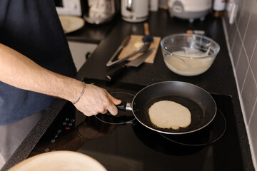 A close-up shot of a man preparing pancakes using a hot frying pan, soft focus.