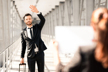 Cheerful businessman waving to assistance with placard, meeting in airport. Handsome middle-aged...