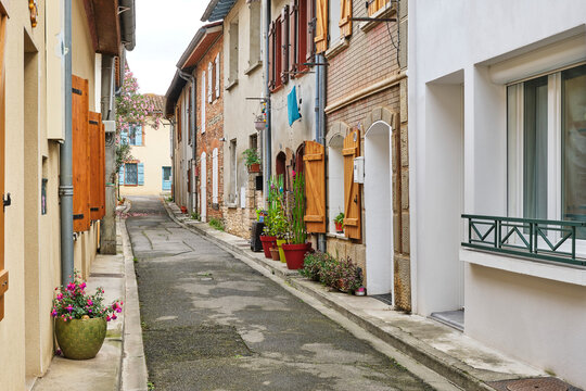 Fototapeta Traditional narrow street in Portet-sur-Garonne in Haute-Garonne Occitanie Southern France with brick and plastered houses with shutters and pots with plants on the street.