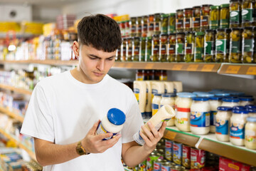 Young man looking to buy jar of mayonnaise in supermarket