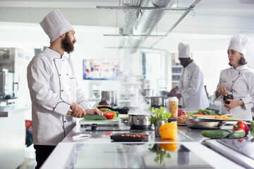 Diverse cooks cutting greenery and fresh vegetables with a knife, preparing ingredients for a new gourmet dish in restaurant kitchen. Professional culinary techniques for a fine dining experience.