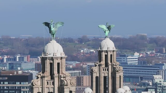 Aerial view of Liverpool with a slow pan showcasing the Liver Building, Anfield Stadium, urban areas, green hills, and a clear blue sky.
