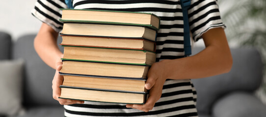 Beautiful female student with stack of books and backpack at home, closeup